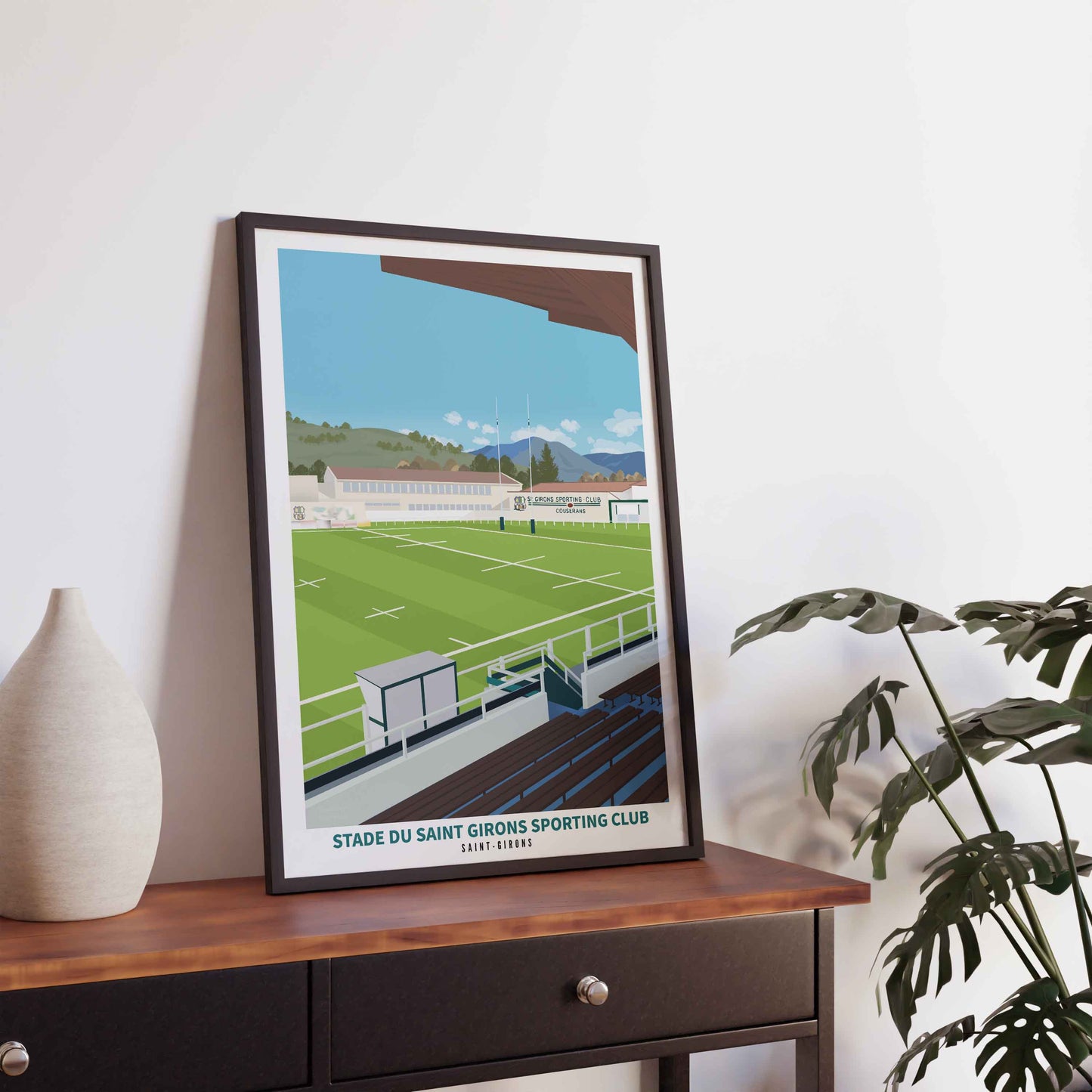 Mise en situation de l'affiche du SGSC dans un cadre noir fin, posée sur une console sombre avec un vase et une plante d'intérieur.