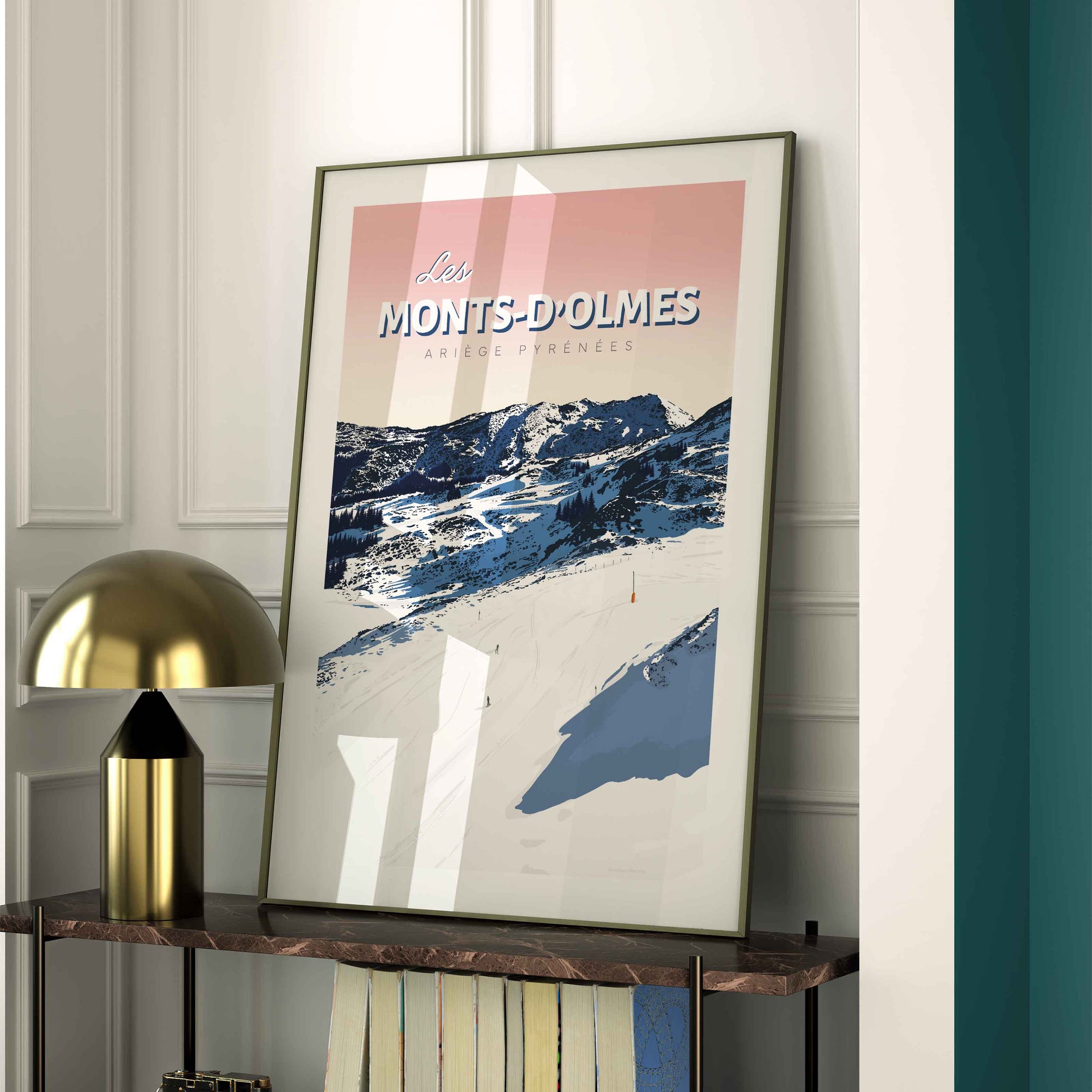 Affiche Les Monts-d’Olmes exposée dans un cadre noir fin sur une étagère moderne, à côté d'une lampe design dorée et d'un mur vert canard.