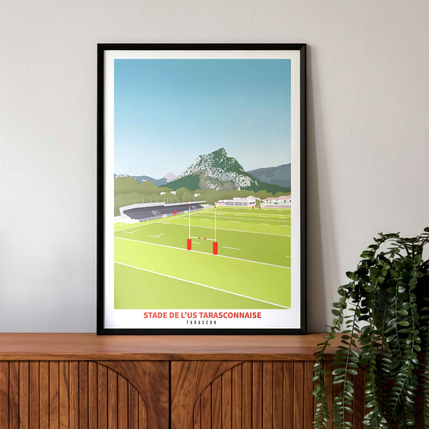 Mise en situation de l'affiche du stade de Tarascon dans un cadre noir, posée sur un buffet vintage en bois avec une plante décorative.
