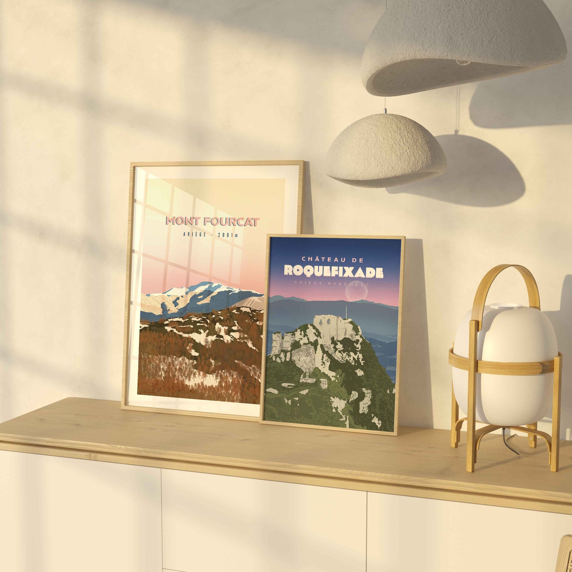 Duo d’affiches de l’Ariège (Mont Fourcat et Roquefixade) posées sur un meuble en bois baigné par la lumière dorée d’une fin de journée.