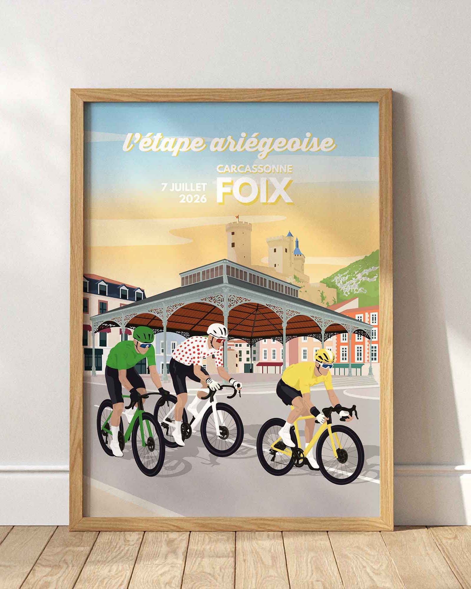 Affiche Foix 2026 illustrant l'arrivée de la Grande Boucle en Ariège devant la Halle aux Grains et le Château de Foix, cadre en bois clair.