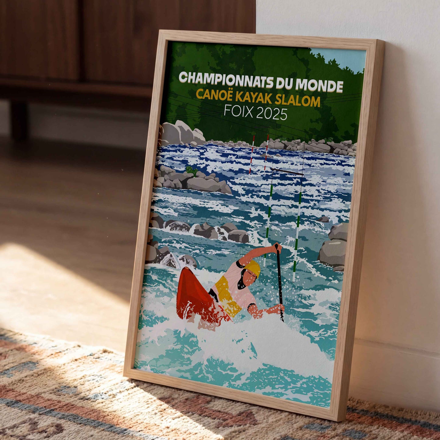 Affiche des Mondiaux de Kayak 2025 à Foix posée verticalement sur un tapis à motifs dans un salon baigné par la lumière du soleil.