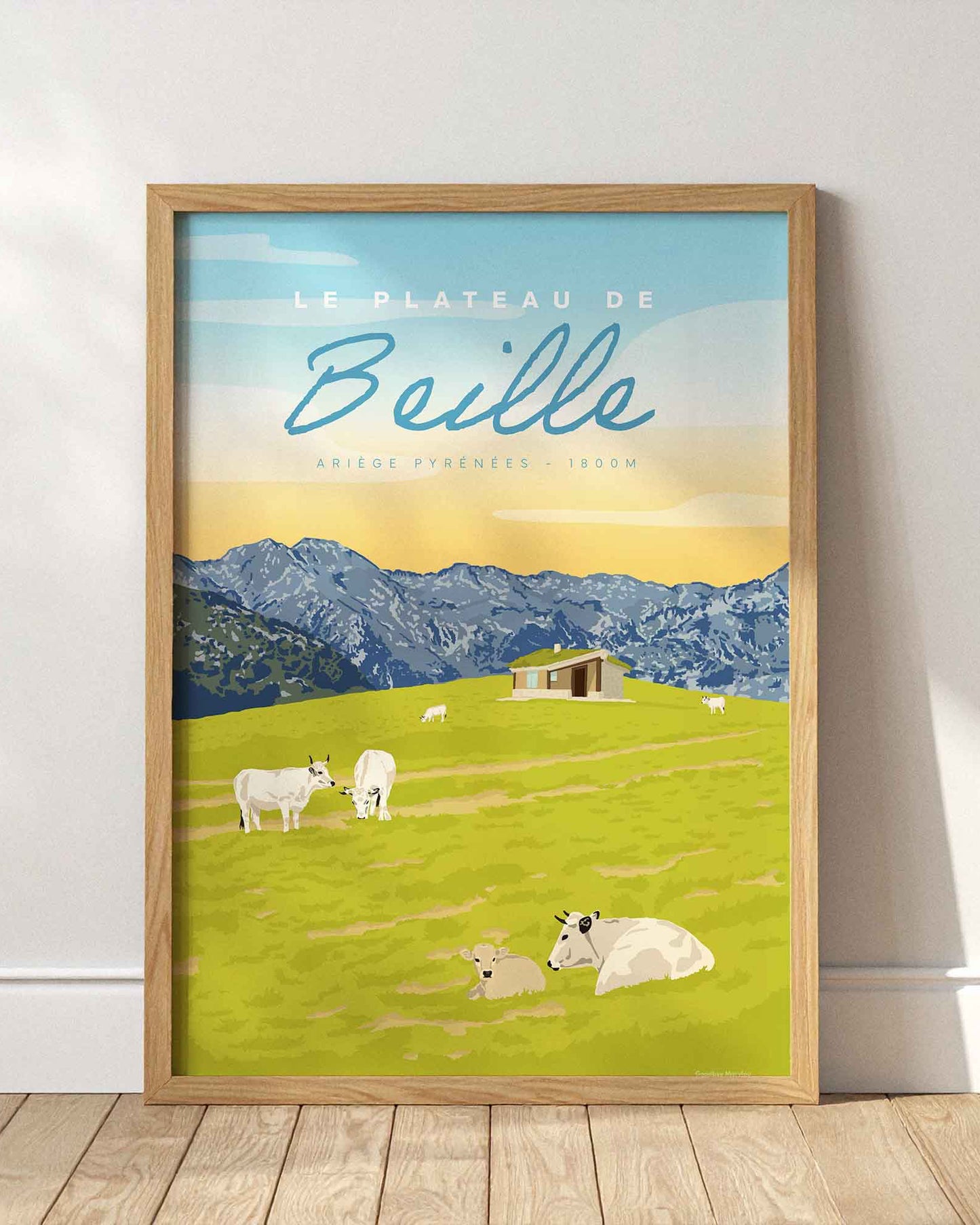 Affiche du Plateau de Beille en été encadrée en bois clair, posée au sol contre un mur blanc épuré avec des jeux d'ombres de fenêtres.