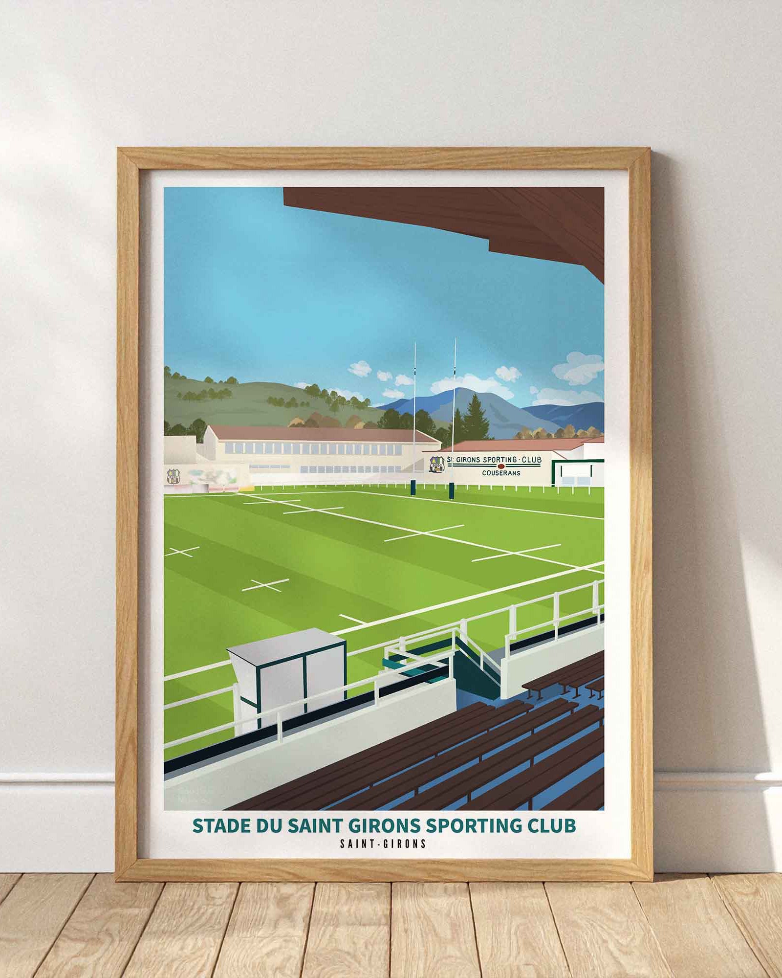 Affiche du stade du Saint Girons Sporting Club encadrée en bois clair, posée au sol contre un mur blanc avec des ombres portées.