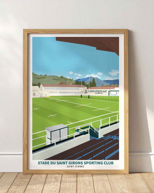 Affiche du stade du Saint Girons Sporting Club encadrée en bois clair, posée au sol contre un mur blanc avec des ombres portées.