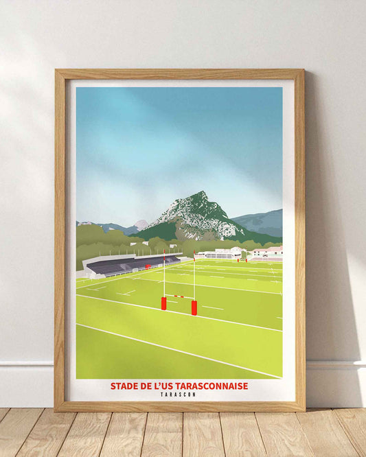 Affiche du stade de l’US Tarasconnaise à Tarascon encadrée en bois clair, posée au sol contre un mur blanc épuré.