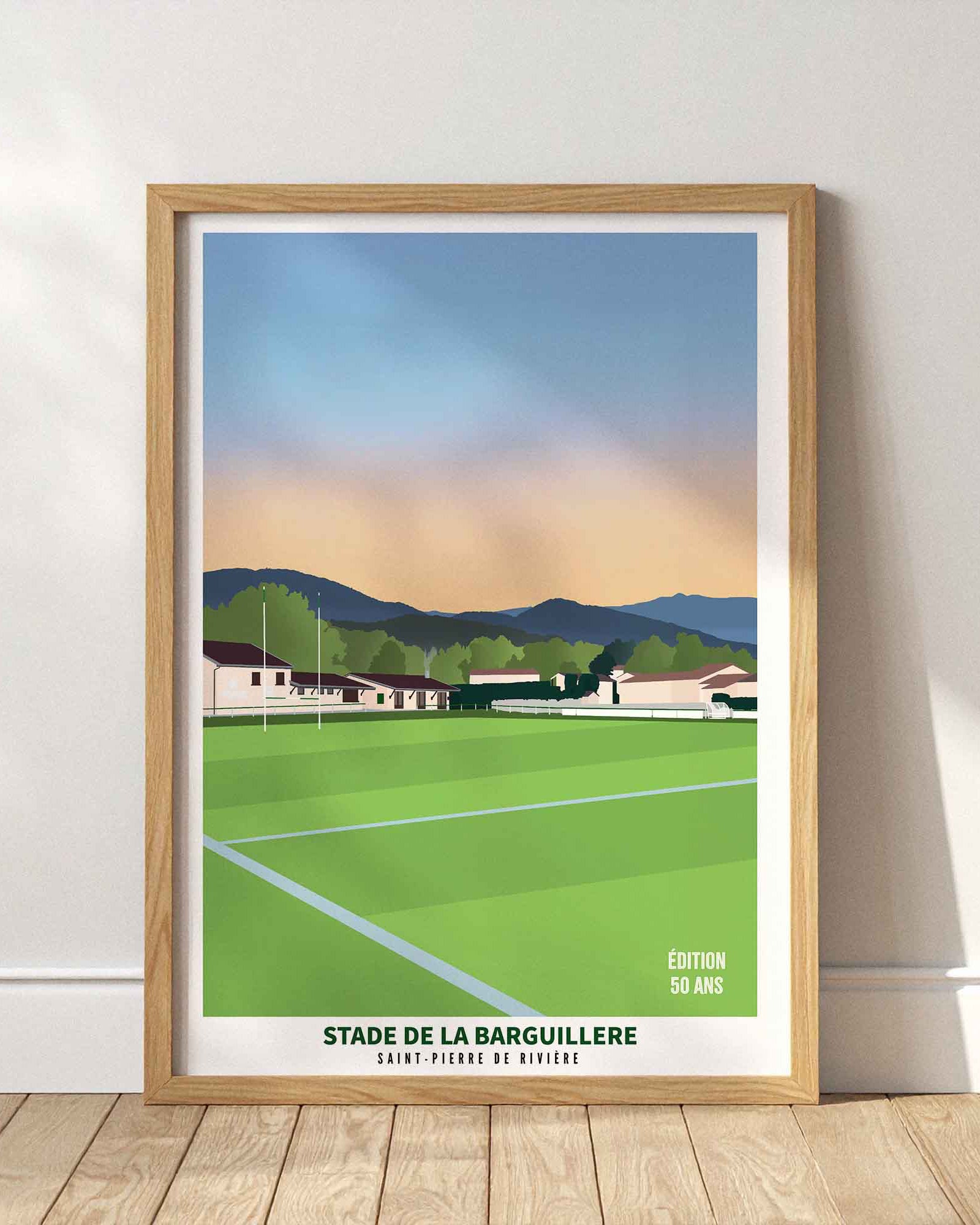 Affiche du stade de la Barguillère à Saint-Pierre-de-Rivière encadrée en bois clair, posée au sol contre un mur blanc épuré.