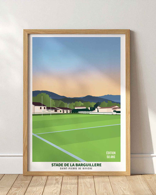 Affiche du stade de la Barguillère à Saint-Pierre-de-Rivière encadrée en bois clair, posée au sol contre un mur blanc épuré.