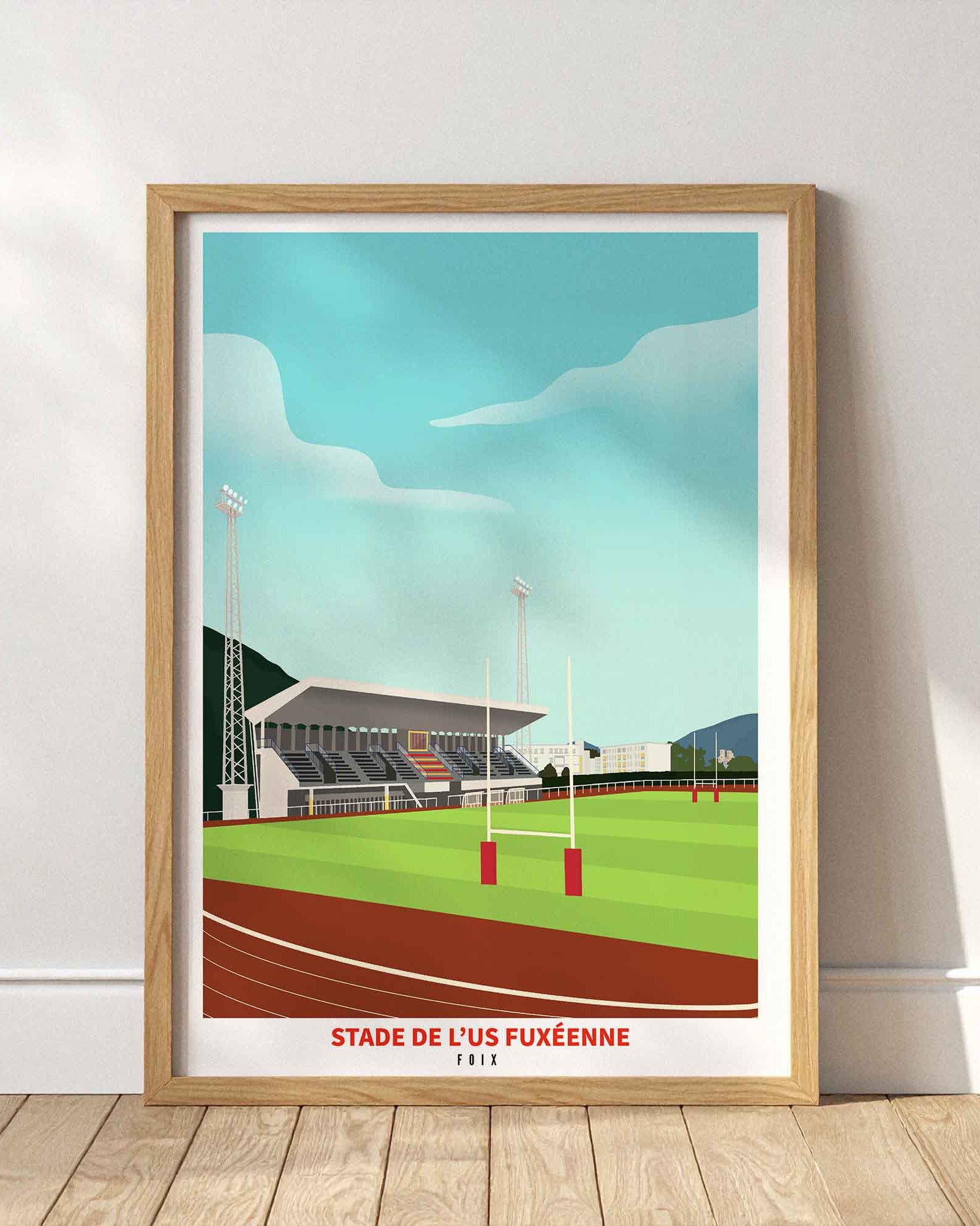 Affiche du stade de l’US Fuxéenne (Foix) encadrée en bois clair, posée au sol contre un mur blanc épuré avec des jeux d'ombres