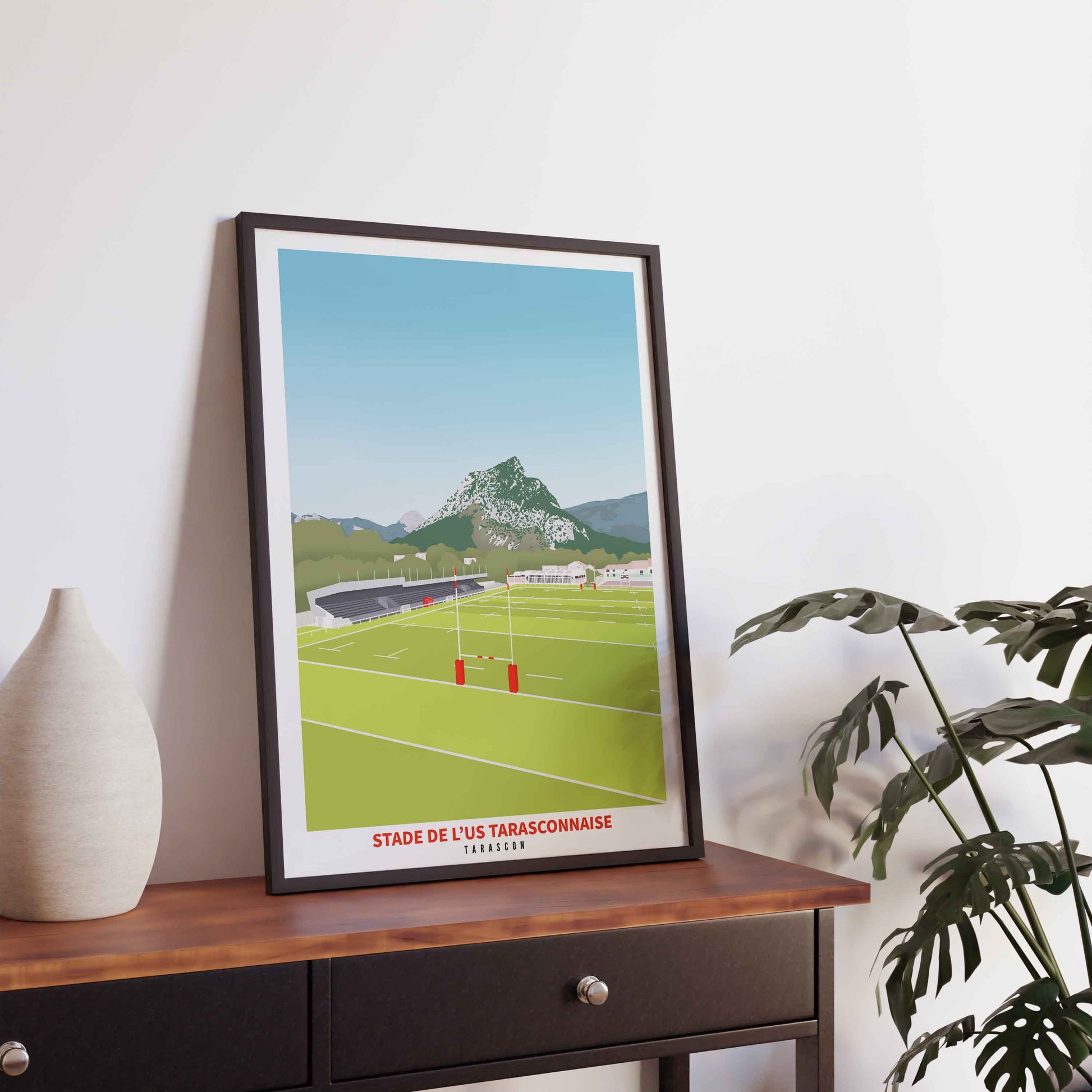 Illustration du stade de rugby de Tarascon avec sa montagne emblématique en fond, dans un cadre noir fin sur une console sombre.
