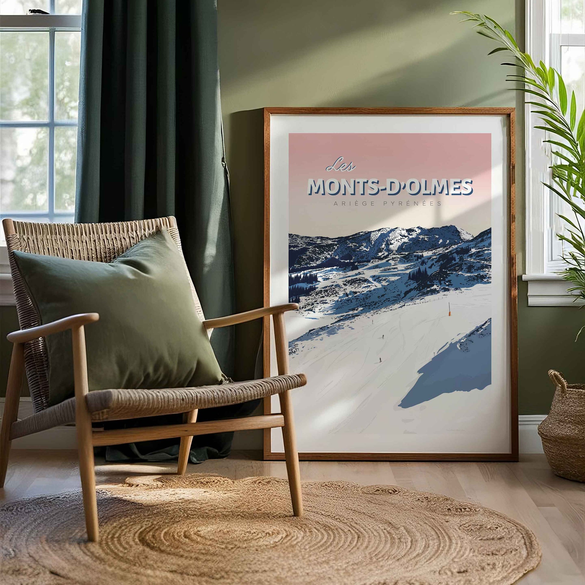 Affiche de montagne ariégeoise dans un cadre en bois, posée au sol dans un coin lecture avec un fauteuil en bois, un coussin vert et une plante.