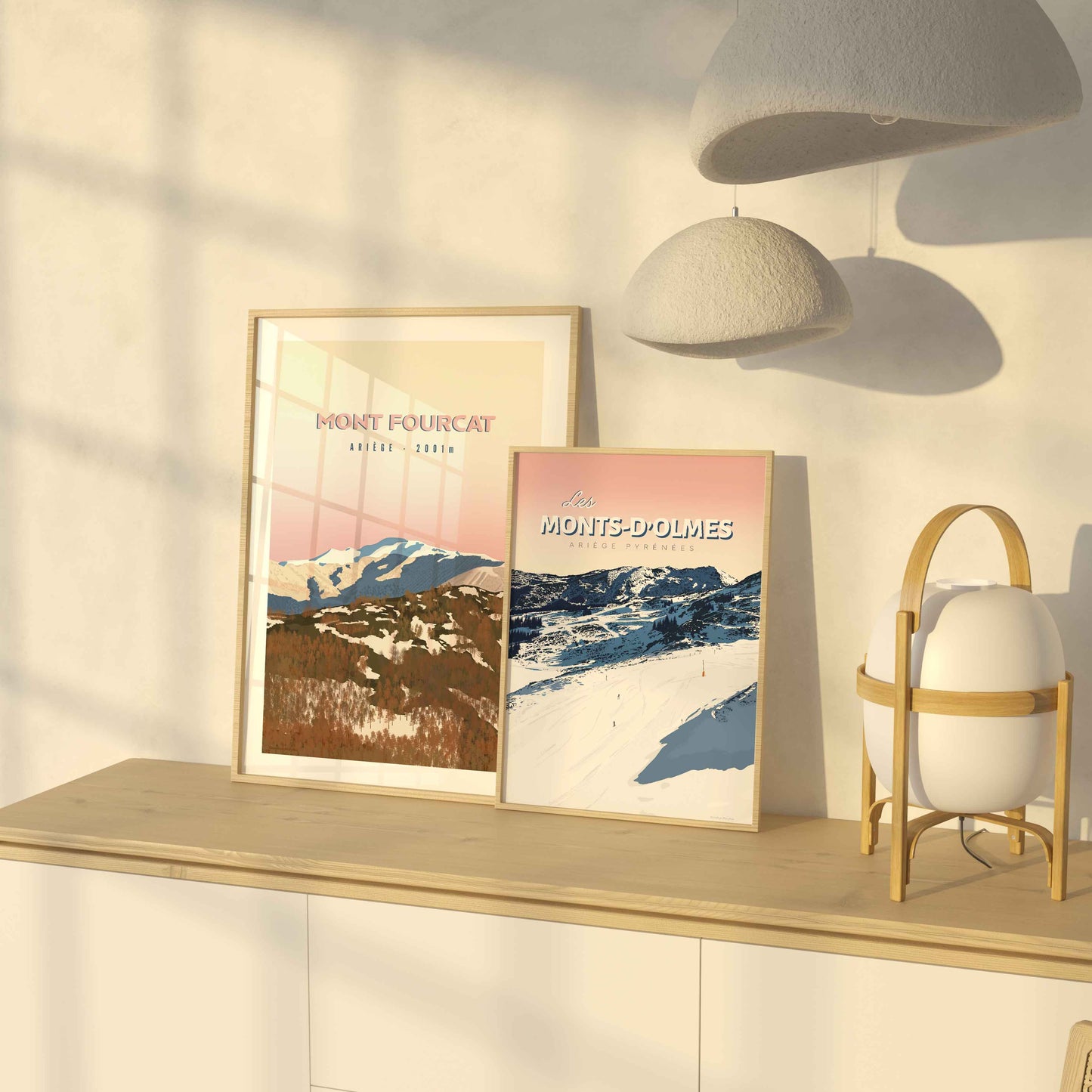 Duo d’affiches de l’Ariège (Mont Fourcat et Monts-d’Olmes) posées sur un meuble en bois baigné par la lumière dorée d’une fin de journée.